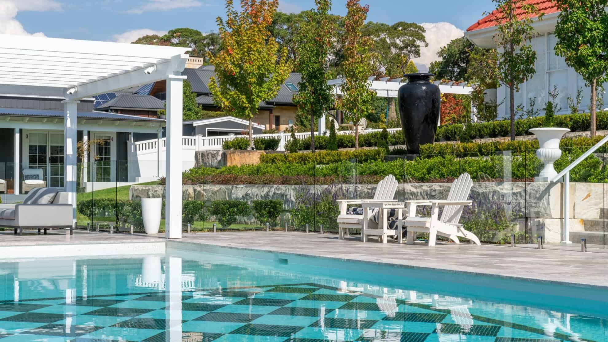Swimming pool with chequered floor beside a pergola lounge and terraced garden